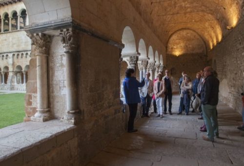 Claustre-del-Monestir-de-Sant-Cugat-1 grup de persones escoltant les explicacions d'una guia al claustre del Monsetir de Sant Cugat del Vallès