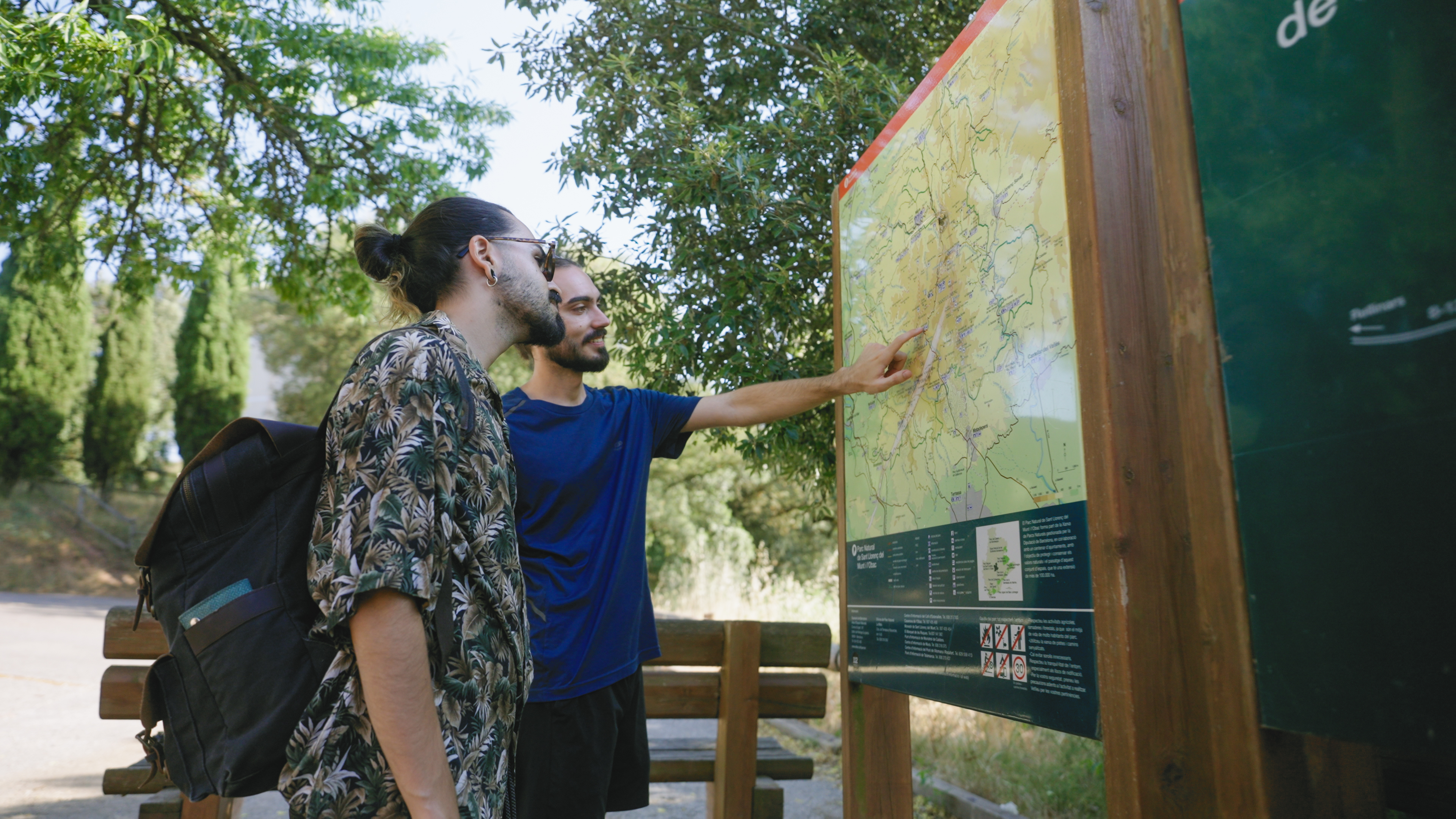 Dos nois joves vestits d’esport mirant un plafó amb el mapa de rutes al Parc Natural de Sant Llorenç del Munt i l’Obac.